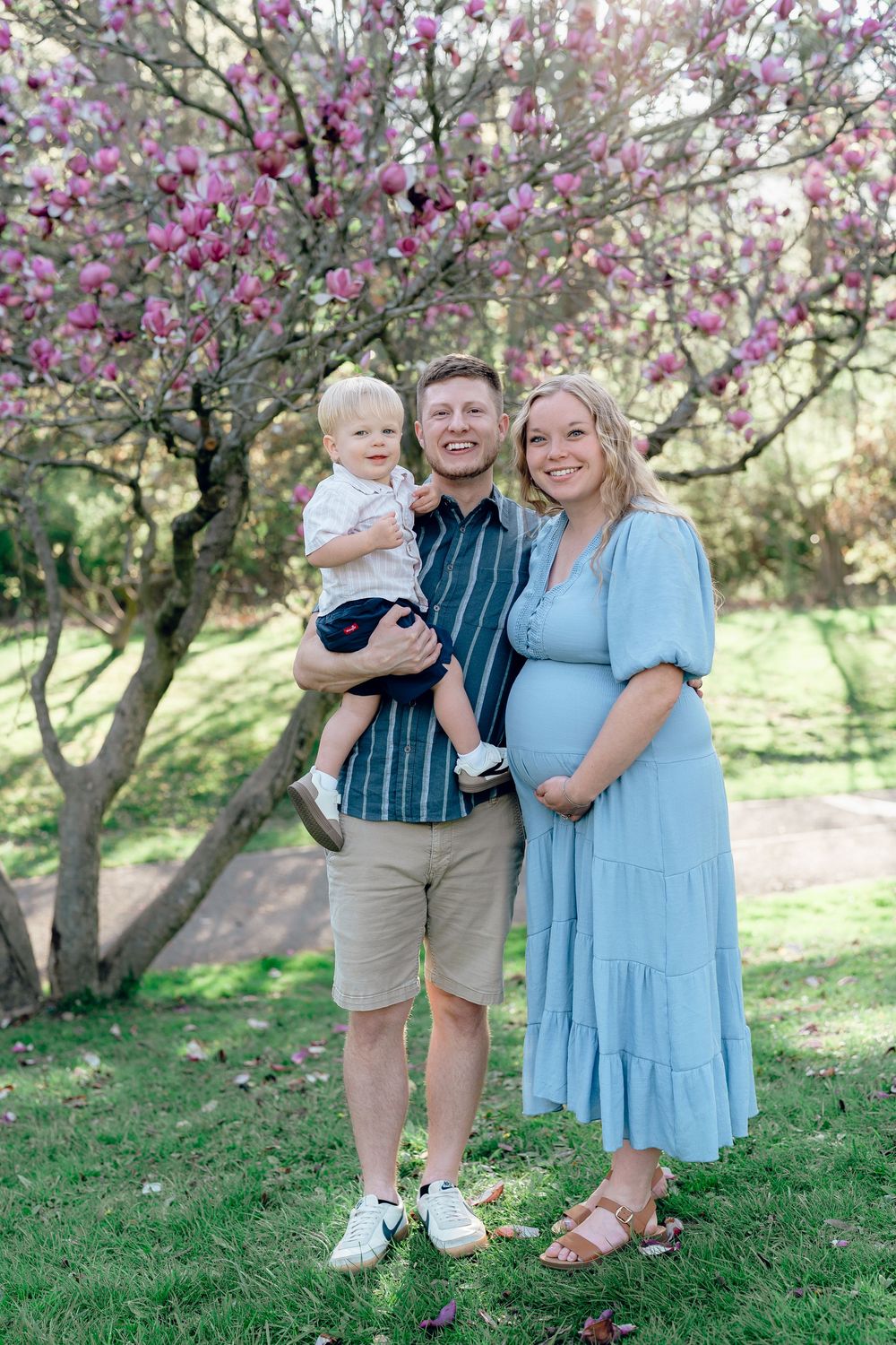 Family standing together under blooming magnolia tree with small child and pregnant mother in blue dress at F.A. Seiberling Nature Realm OH
