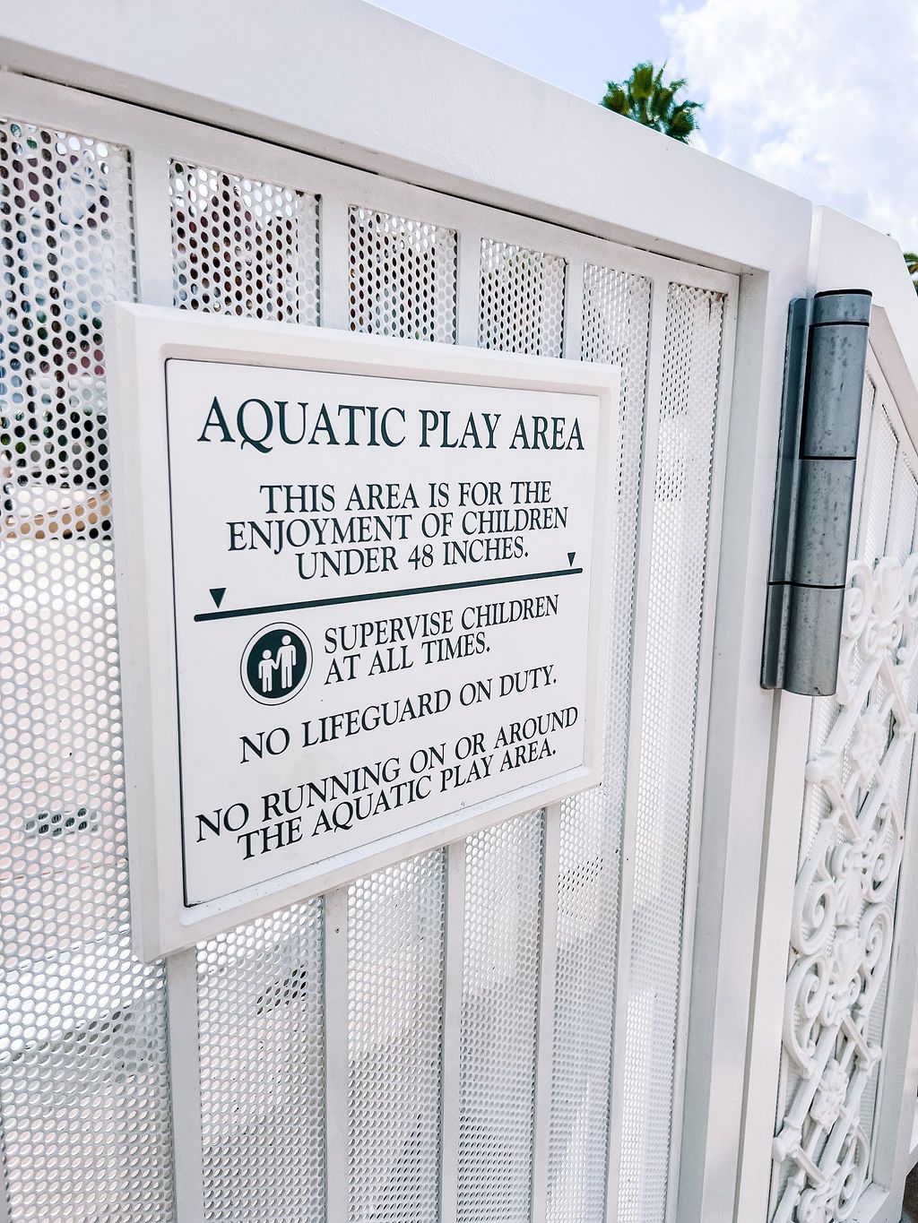 White metal gate with aquatic play area rules and safety guidelines sign.