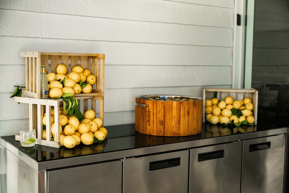Fresh yellow grapefruit displayed in wooden crates and glass containers on stainless steel counter.