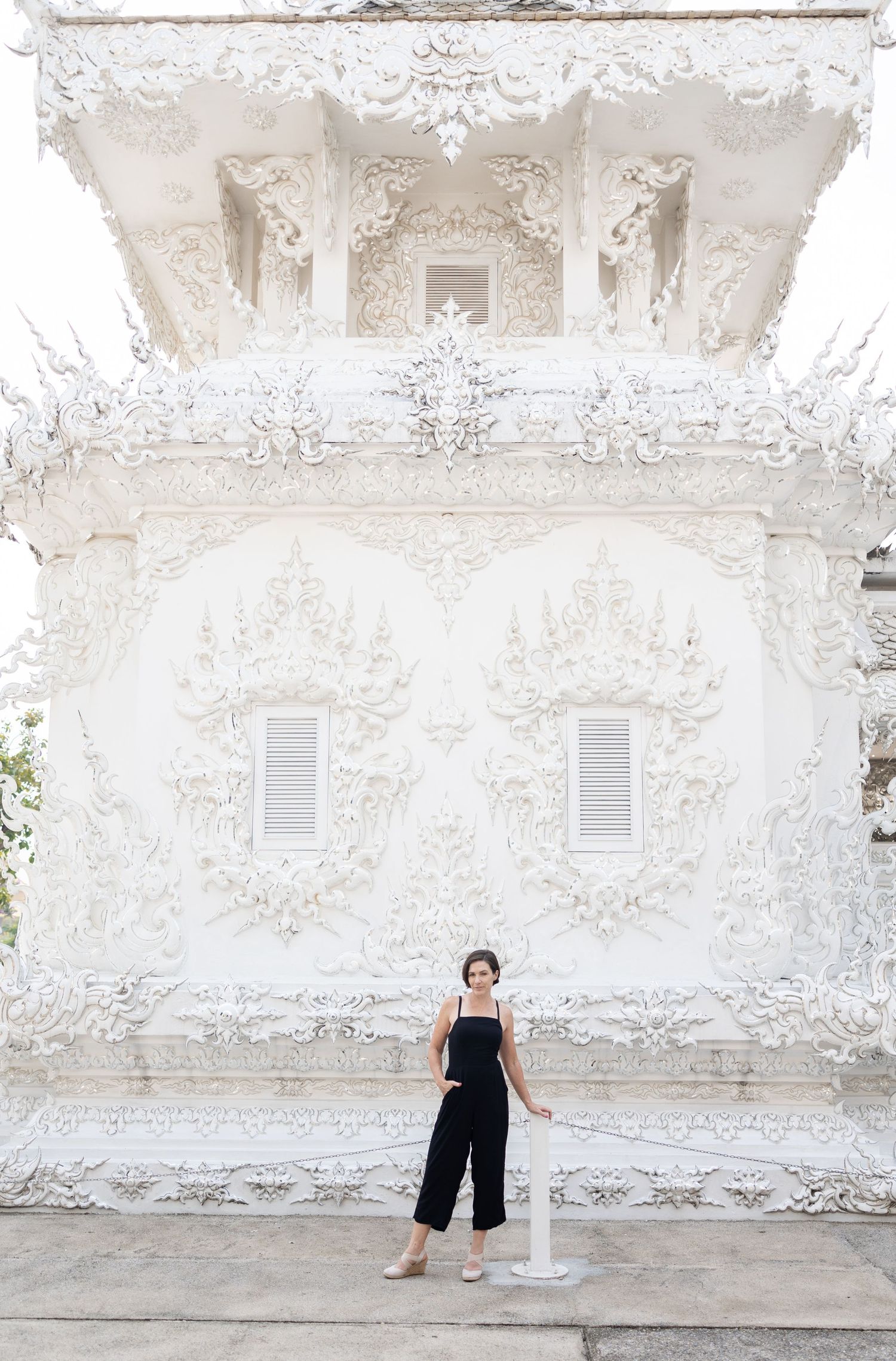 A white ornate temple wall with intricate architectural details serves as a backdrop for a stylish photo.