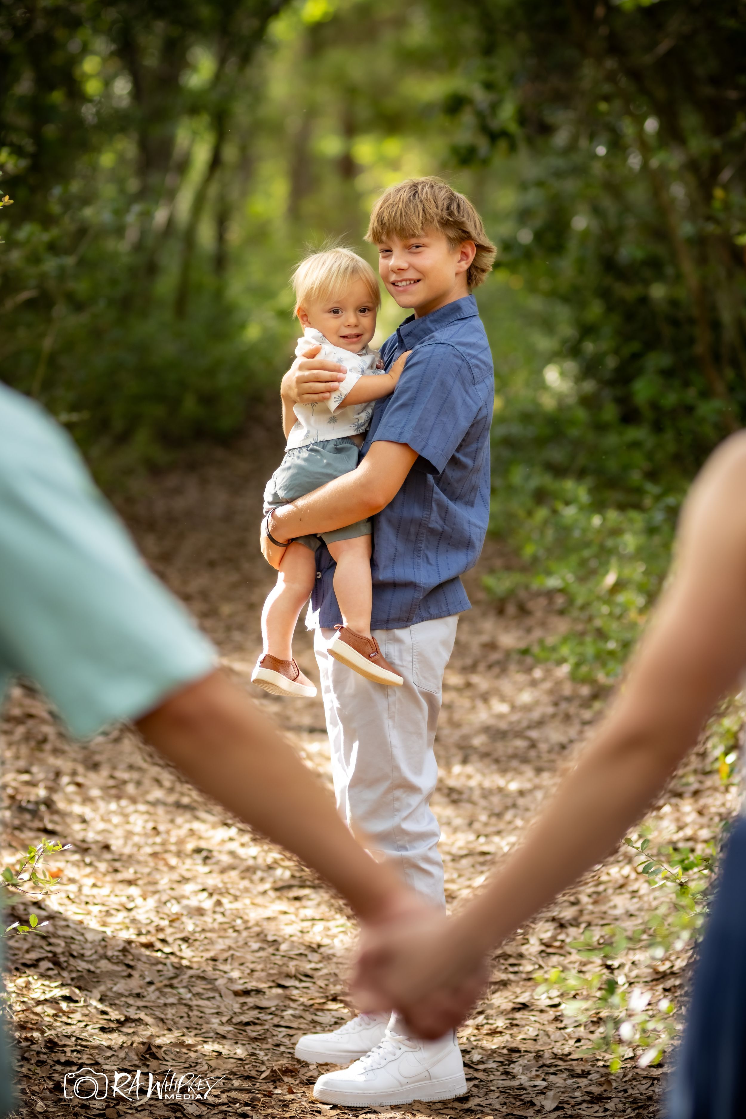 Brothers sharing a sweet moment together on a wooded nature trail as others hold hands in the foreground.