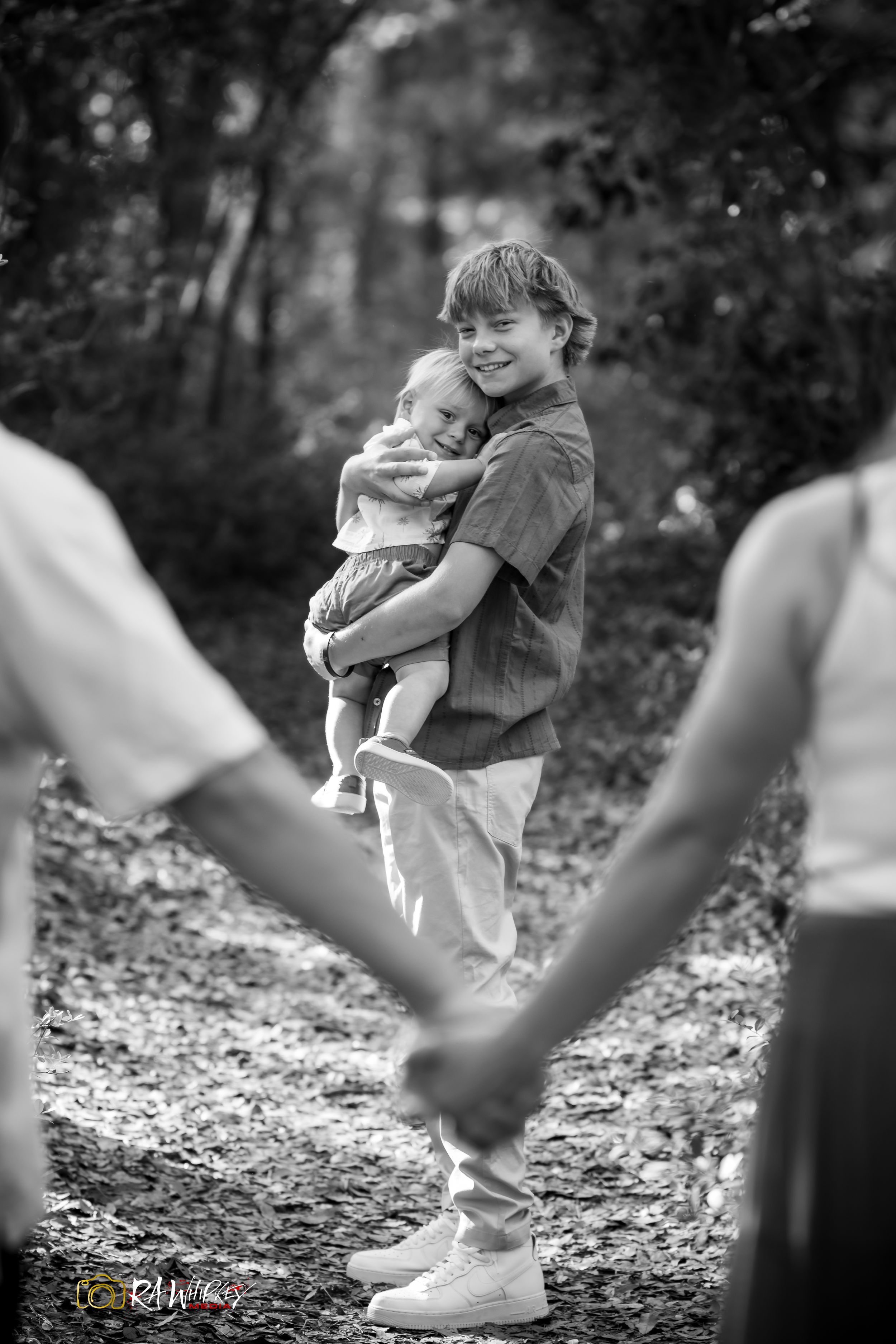 Creative black and white photograph showing two people in the background holding hands forming a heart shape around a figure.
