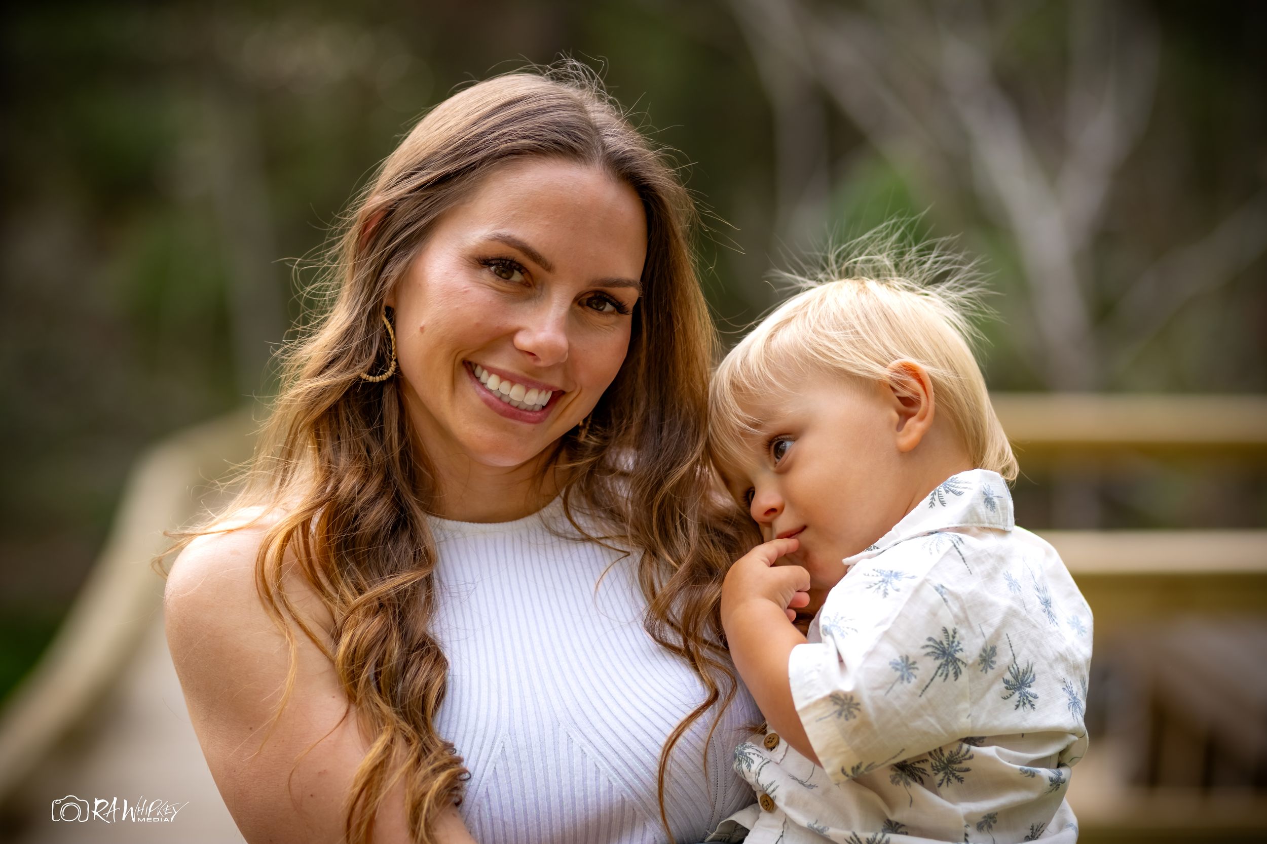 A parent and toddler share tender outdoor moments with their fluffy white dog while wearing casual summer attire.