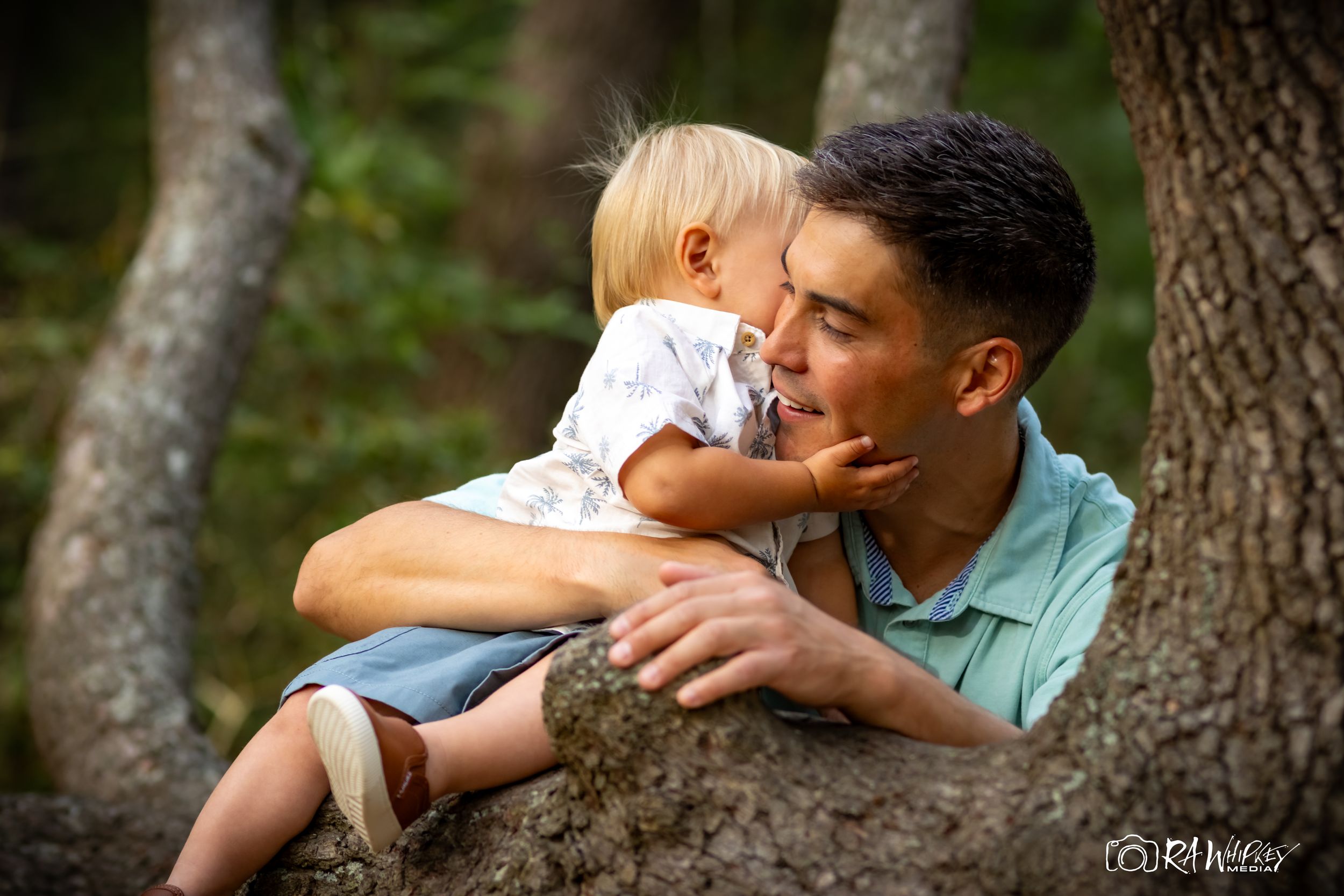 A tender moment between adult and child sharing an affectionate embrace outdoors among trees.