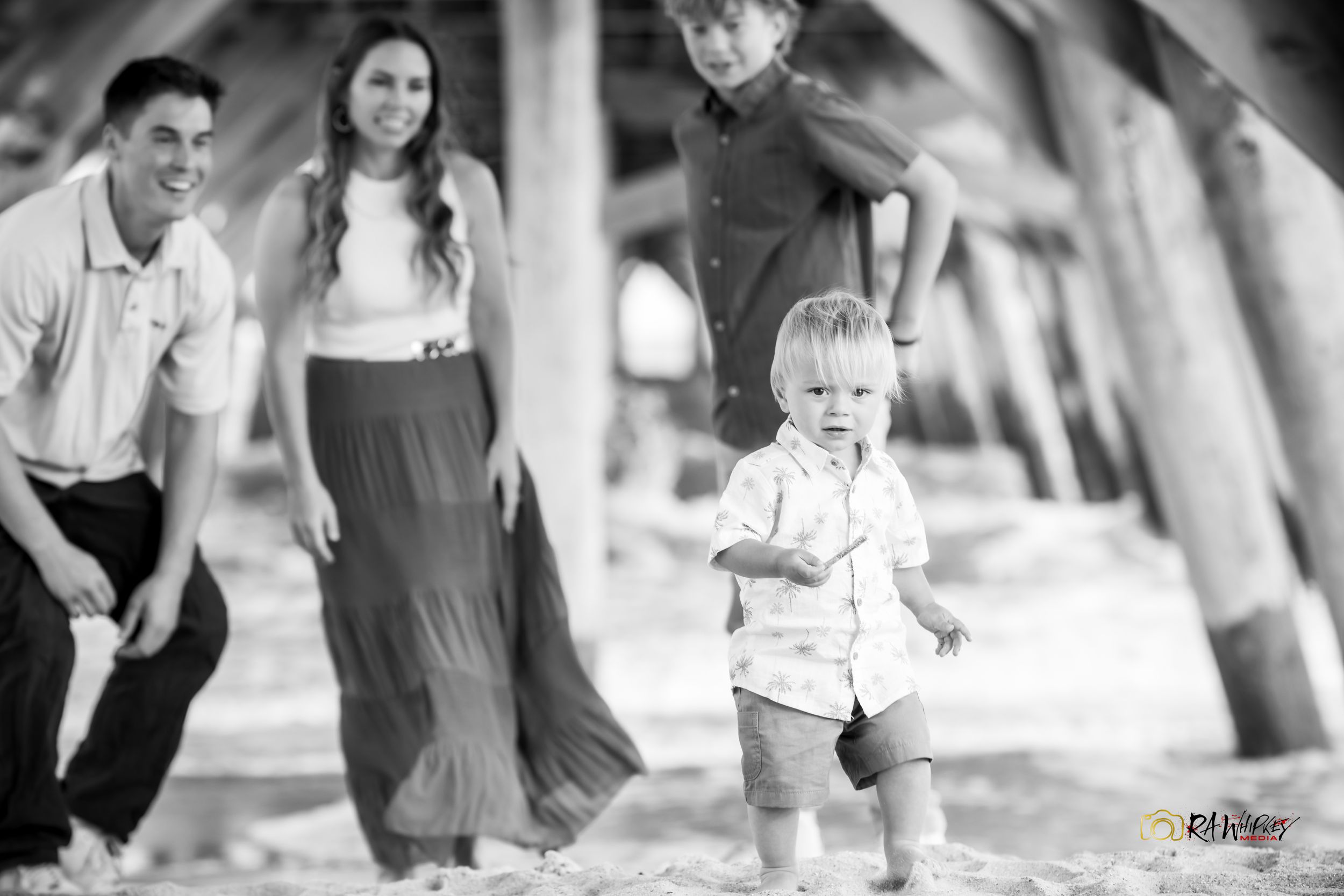 Black and white family portrait captured outdoors under shady trees with casually dressed subjects.