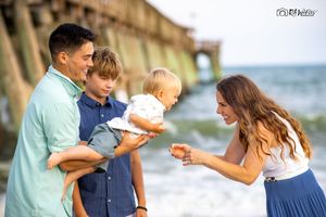 A family shares a joyful moment together on a sunny beach with an ocean and bridge in the background.
