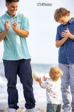 Three people dressed in casual clothing standing together and praying on a beach.
