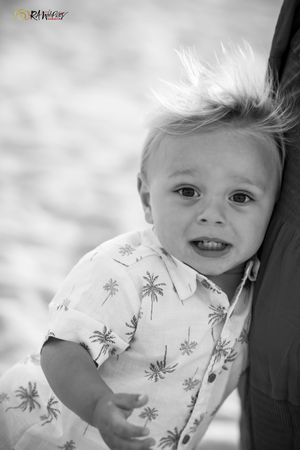 Black and white portrait of a child with spiked hair wearing a palm tree print shirt smiling at the camera.
