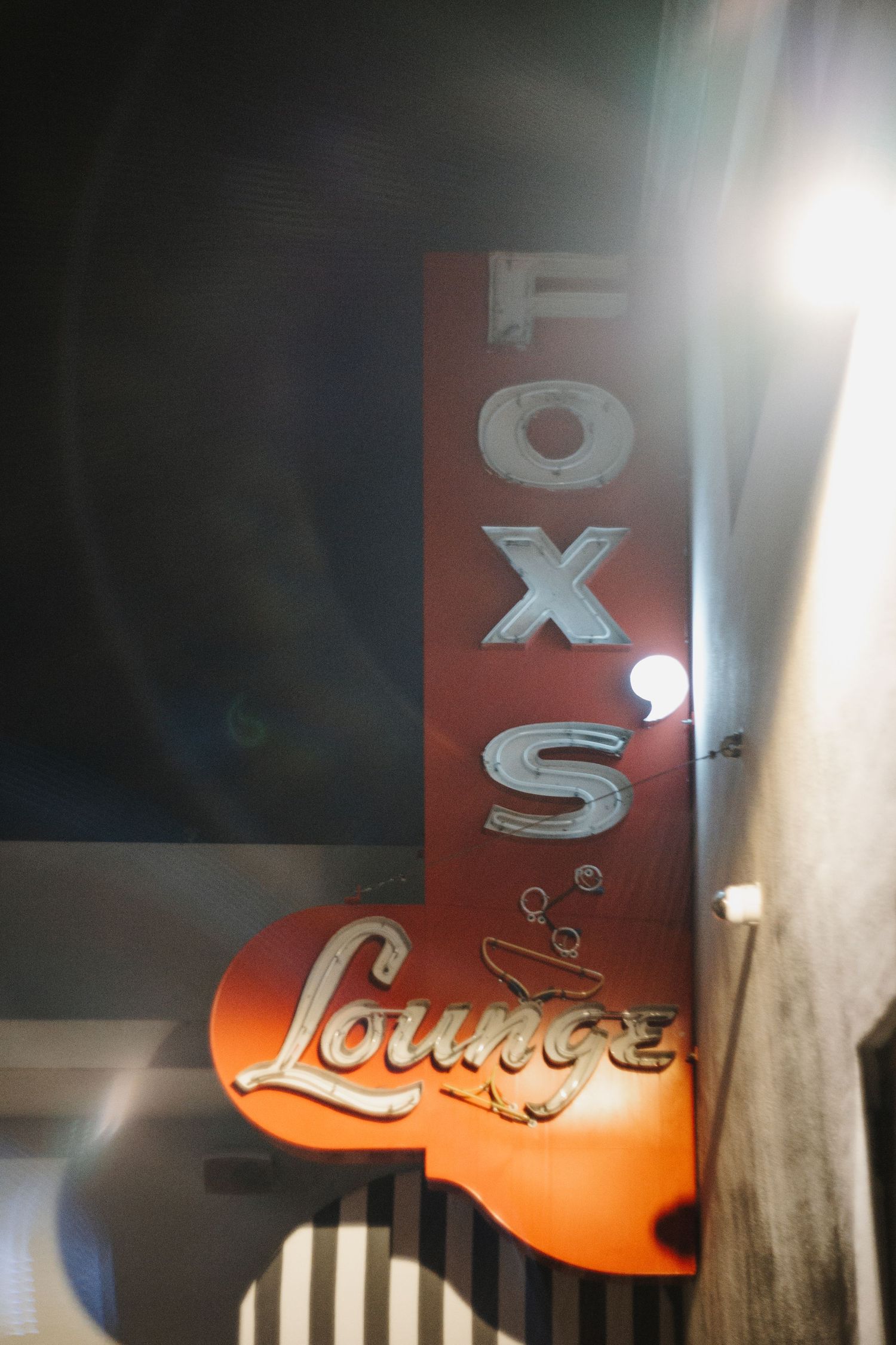 Illuminated orange lounge sign letters mounted on wall with dramatic lighting and shadow effects create ambient atmosphere.
