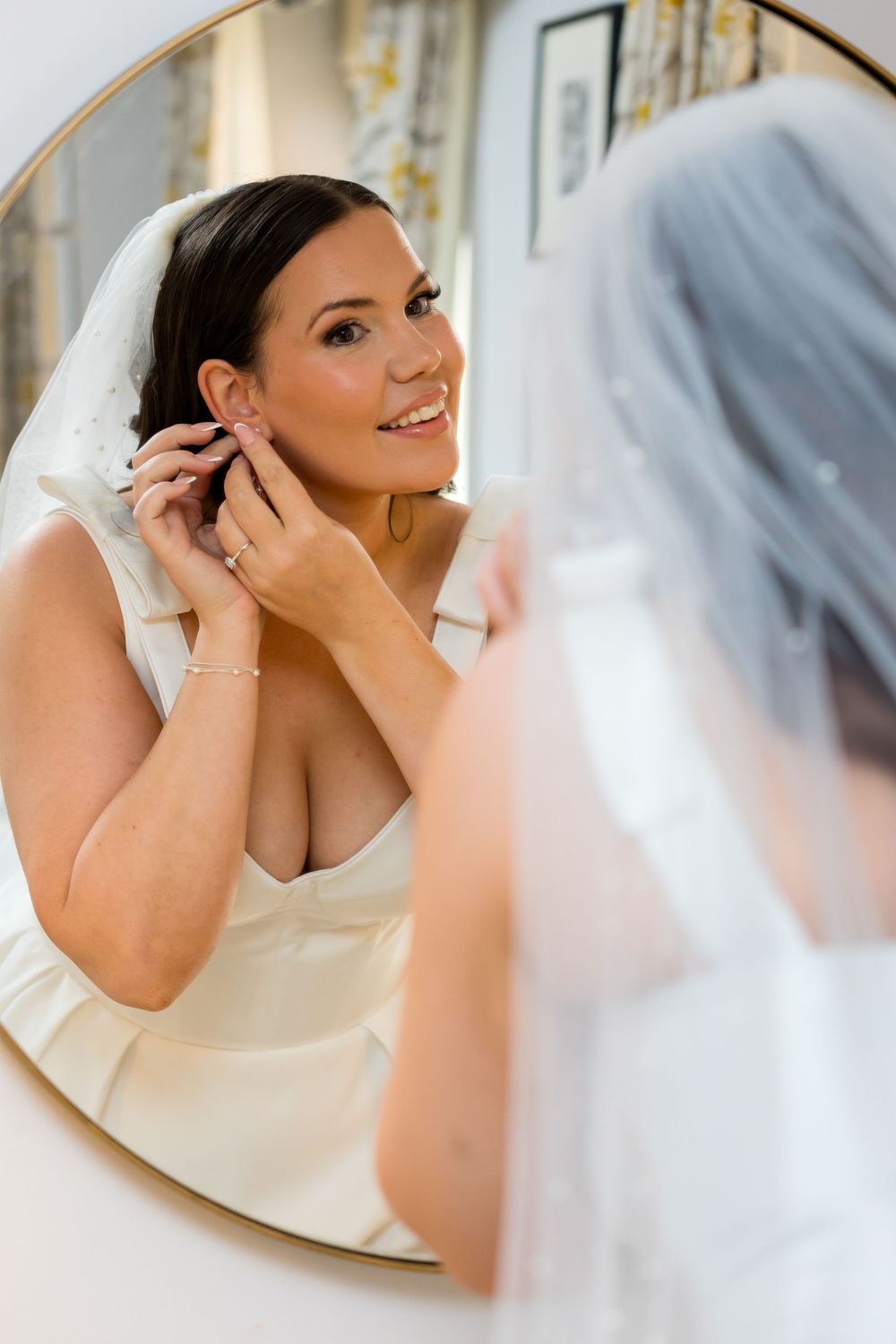Bride smiling in the mirror while putting on earrings before the wedding ceremony.