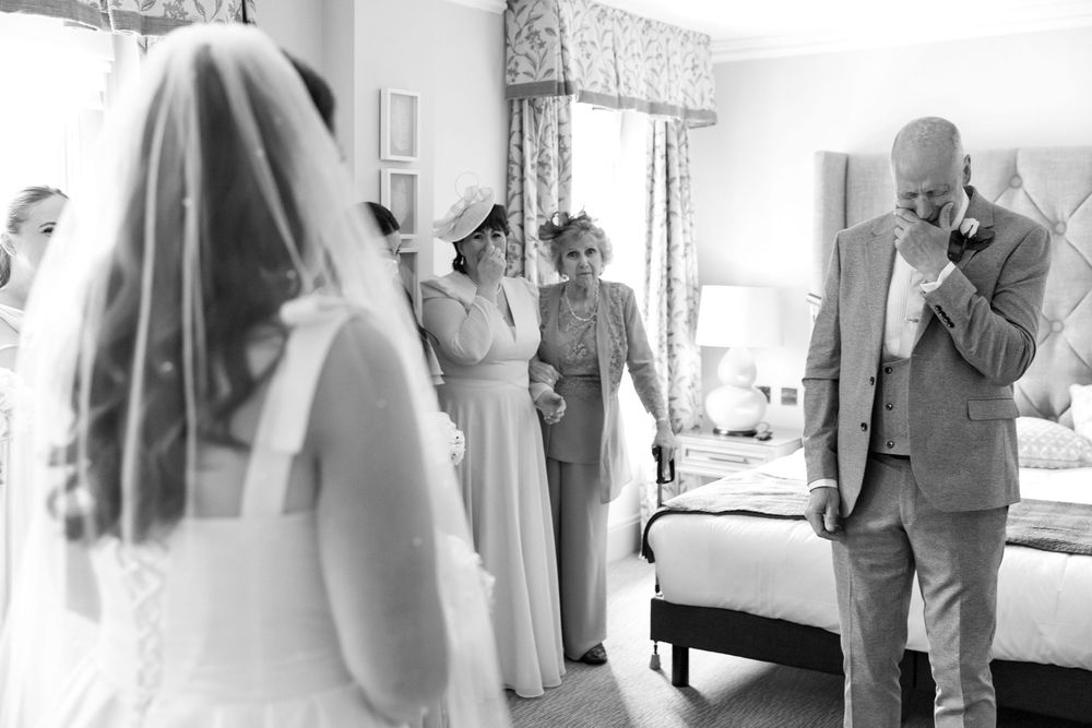 Emotional father of the bride wipes tears during the reveal, surrounded by family.