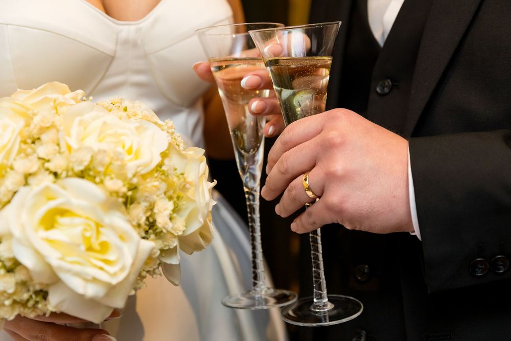 Newlyweds clinking champagne glasses with a white rose bouquet