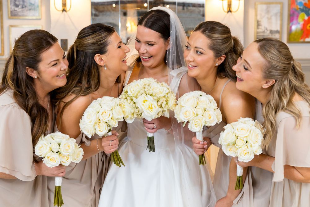 Bride laughing with bridesmaids holding white rose bouquets
