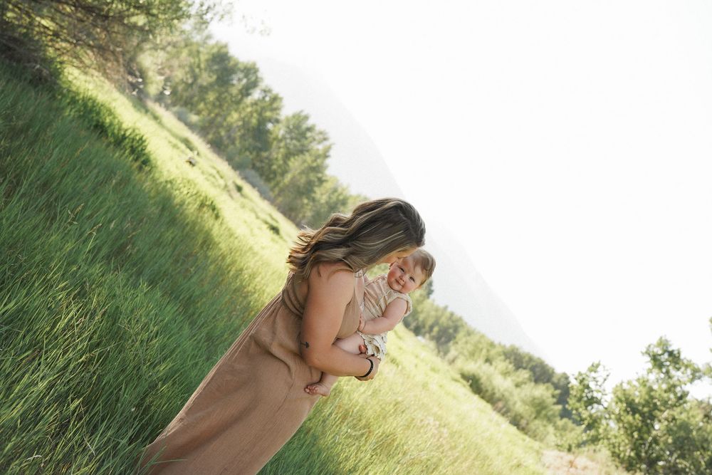 Someone lying on a grassy slope in a meadow against a bright sunny sky with trees in the background.