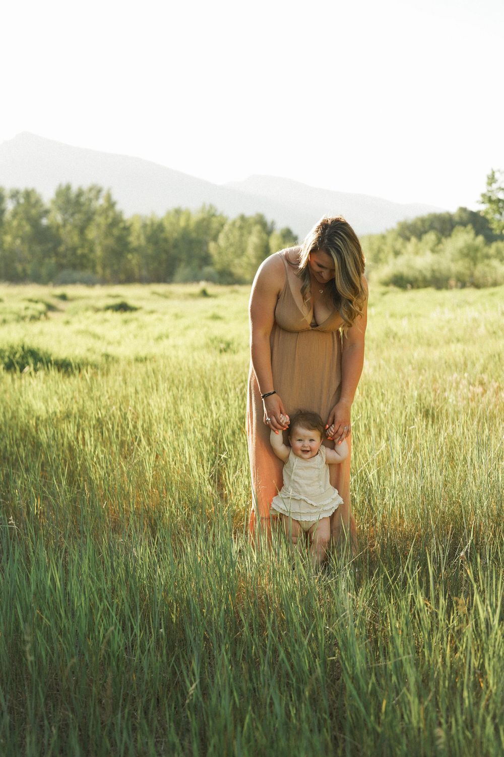 A sweet summer moment in a sunlit meadow with tall grass and mountains in the background.
