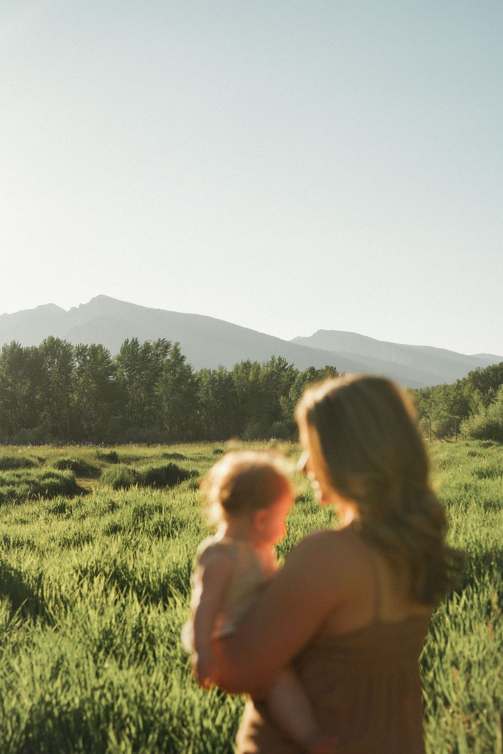 A scenic mountain view at sunset with people enjoying nature in a grassy meadow surrounded by trees.