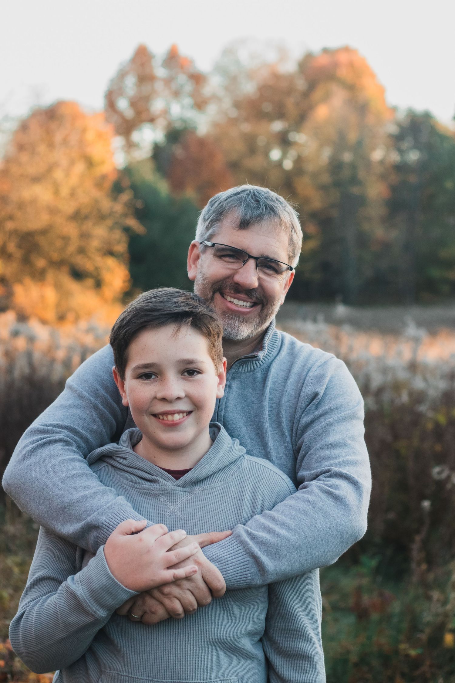 Father with arms around his son during autumn golden hour - Michigan lifestyle faimily photographer captures joyful moments.