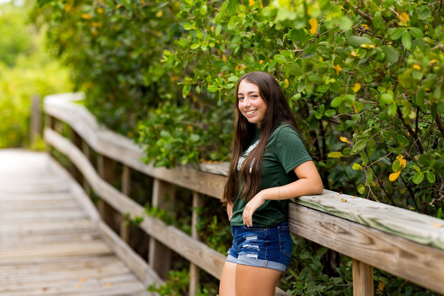 Woman leaning against wooden railing on boardwalk surrounded by green foliage.