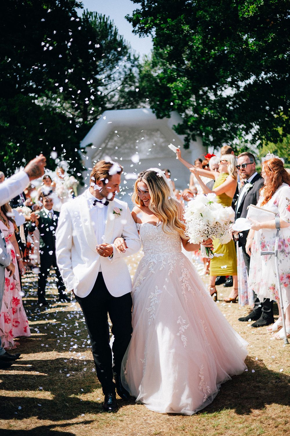 Wedding guests shower the newlyweds with white confetti as they walk through a joyful outdoor celebration.