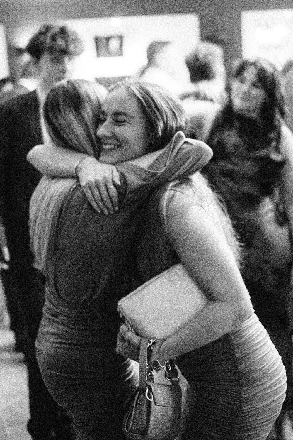 Two women sharing a warm embrace and smiling at a social gathering in black and white photo.