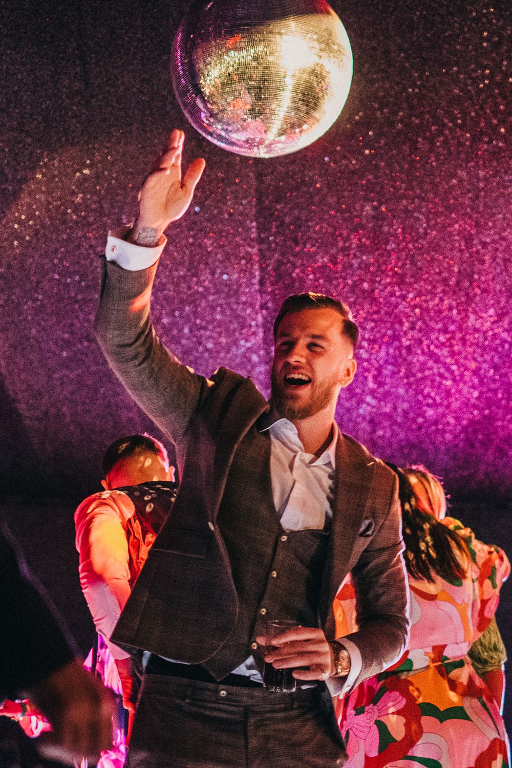 A suited guest reaches for a disco ball during a wedding reception with pink lighting.