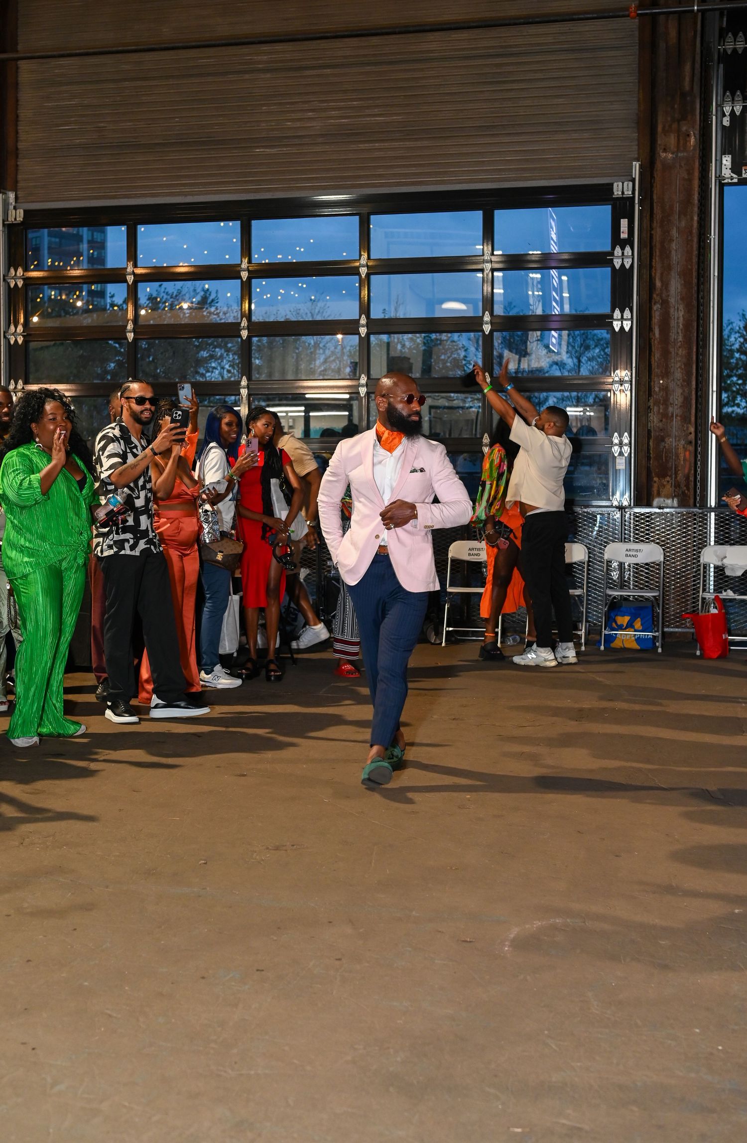 A group of costumed dancers performing in a spacious industrial-style venue with large windows and concrete floors.