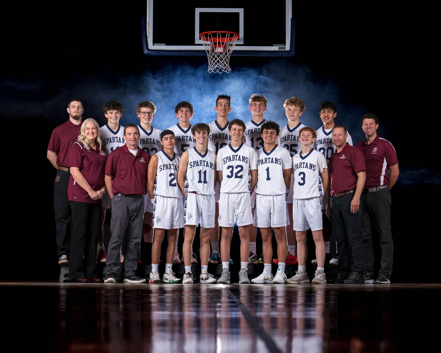 Basketball team stands on court posing for official team photo with coaches in maroon shirts on sides.