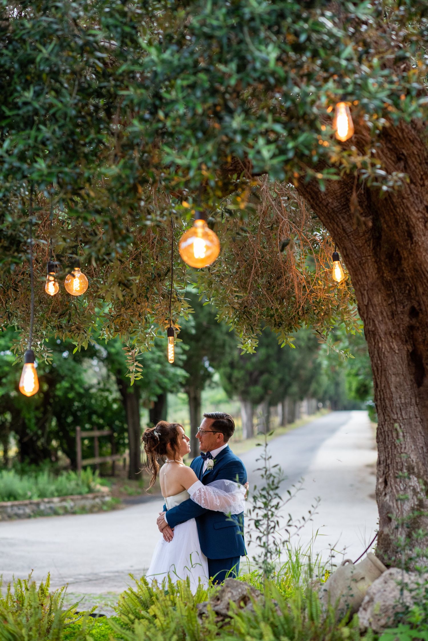 Romantic evening wedding photos under trees decorated with hanging Edison bulbs.