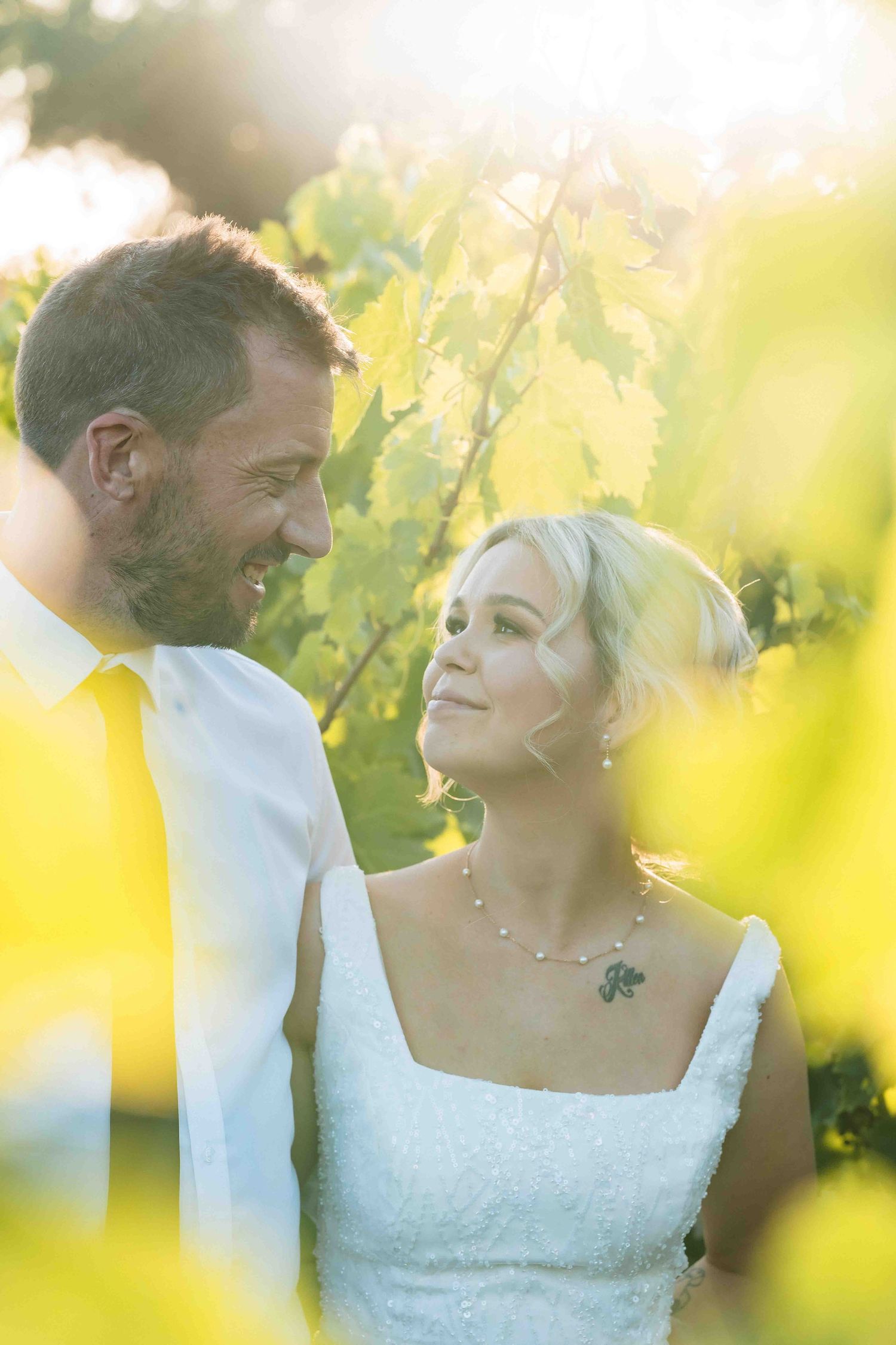 A tender moment between newlyweds amid sunlit vineyard leaves.