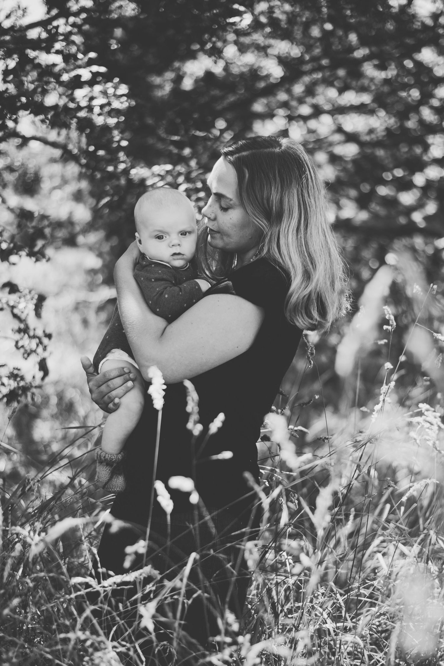 Mother gently holding her baby in a peaceful, sunlit meadow.