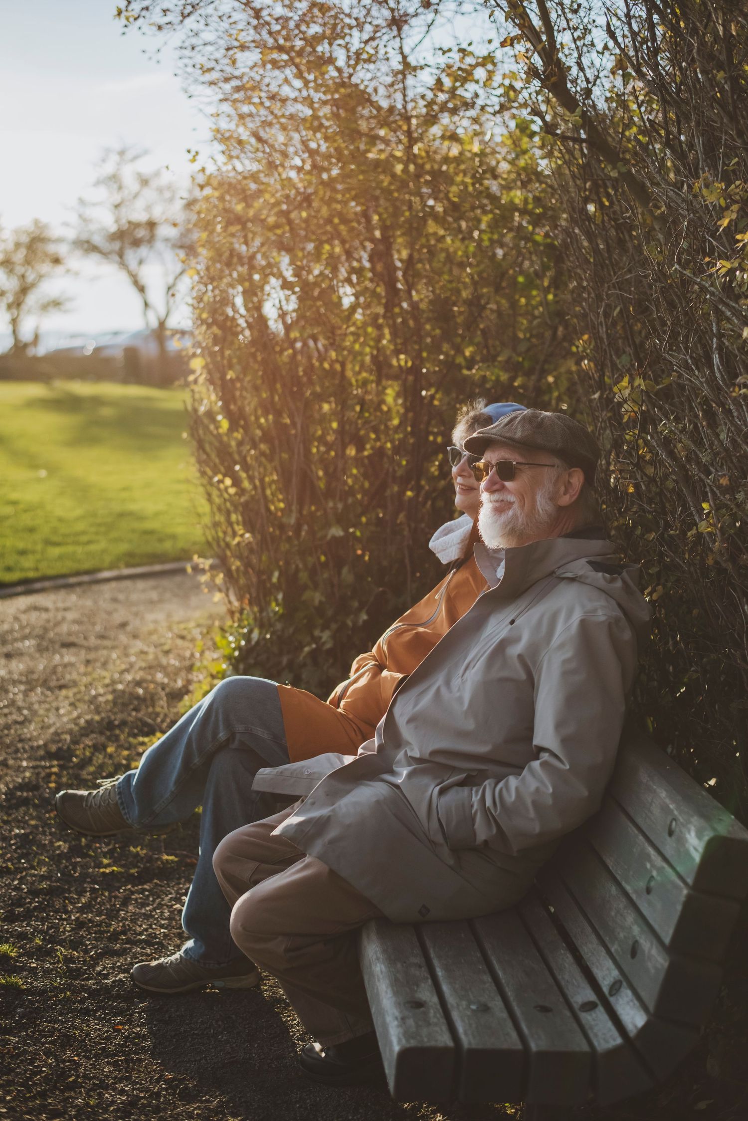 Older couple sitting on a park bench, enjoying a sunny day and the warmth of the afternoon light.