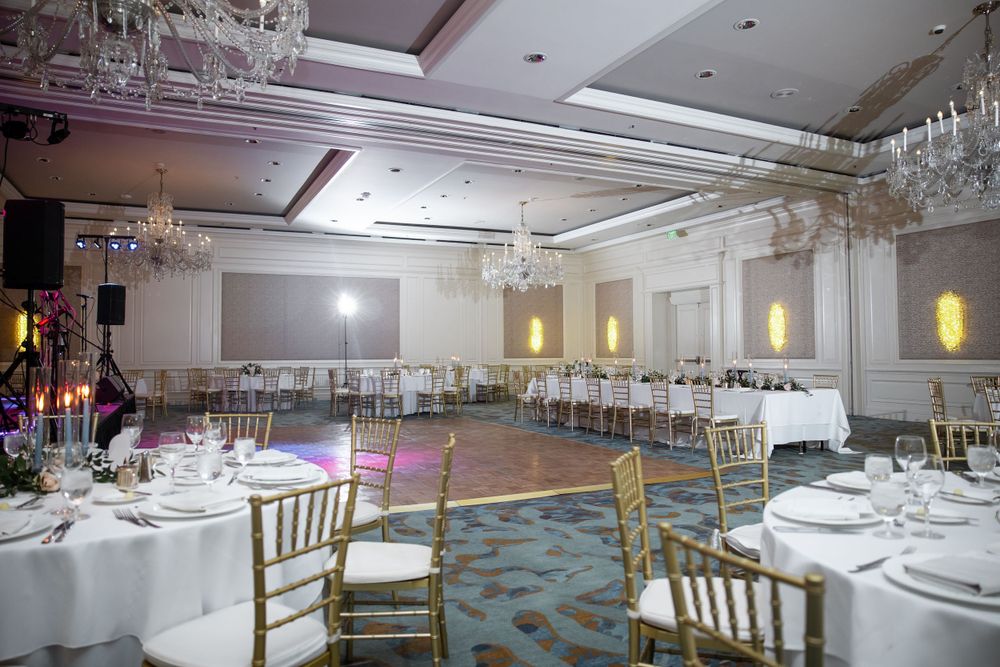 Elegant ballroom setup with round tables, gold chiavari chairs, and crystal chandeliers.