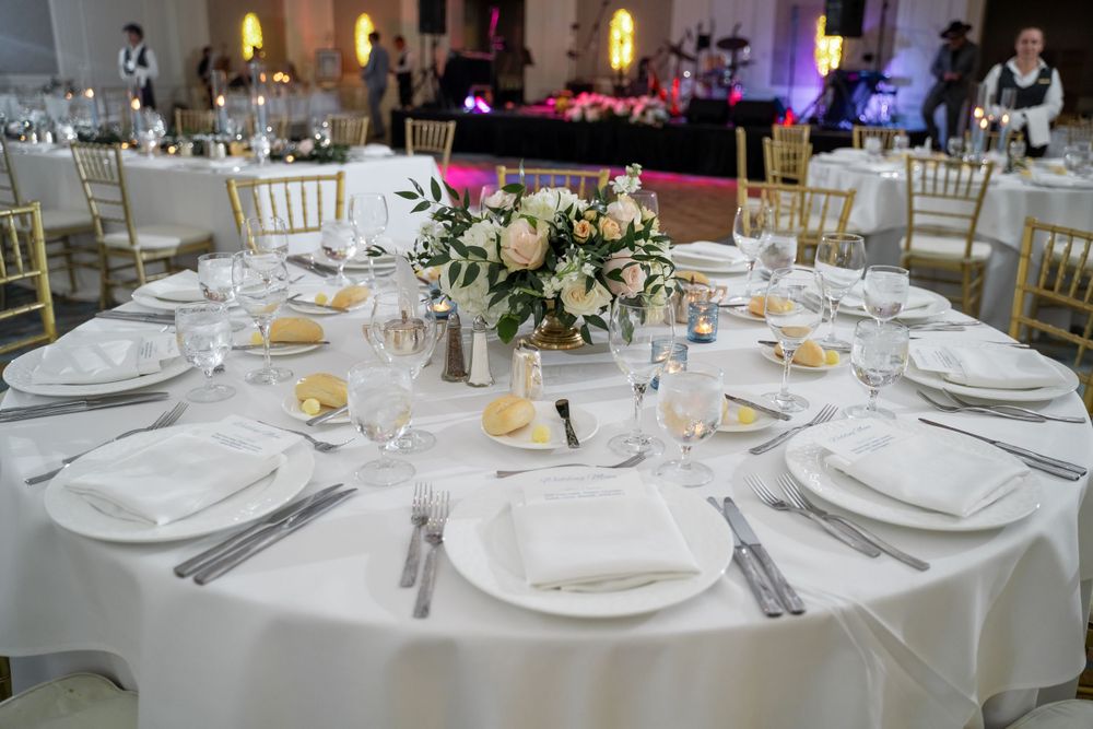 Formal wedding reception table setting with white linens and floral centerpiece.