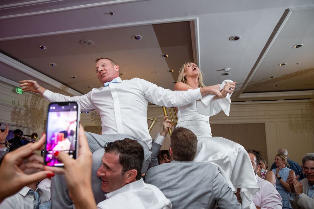 Energetic wedding reception moment with guests lifting celebrants on the dance floor.