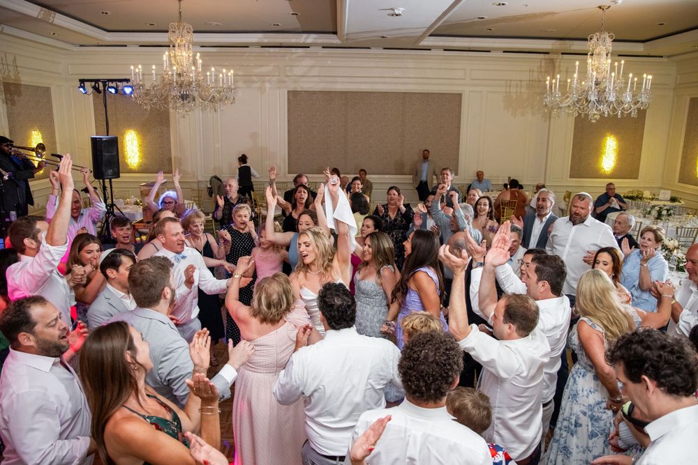 Packed dance floor at wedding reception with guests celebrating under crystal chandeliers.