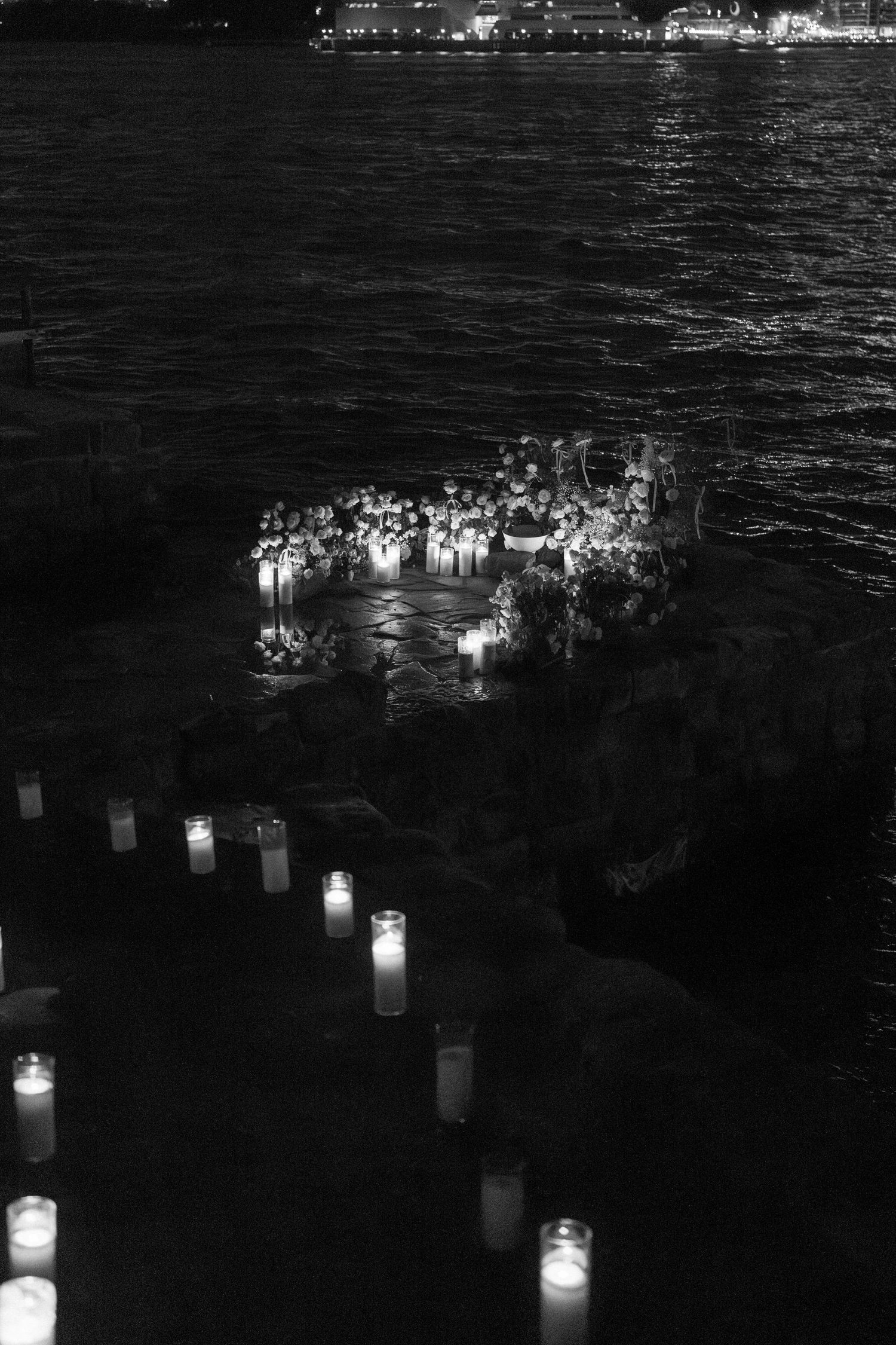 Glowing luminaries or paper lanterns arranged in rows create a peaceful nighttime display over dark water.