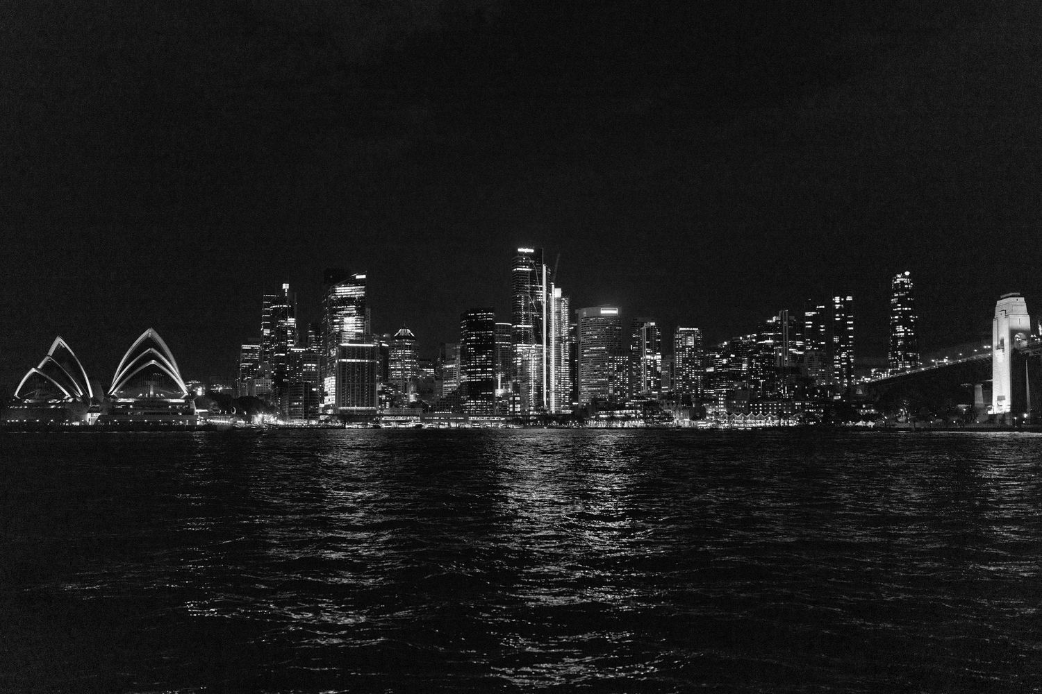 Night skyline of Chicago reflecting on Lake Michigan with illuminated skyscrapers and city lights glowing in darkness.