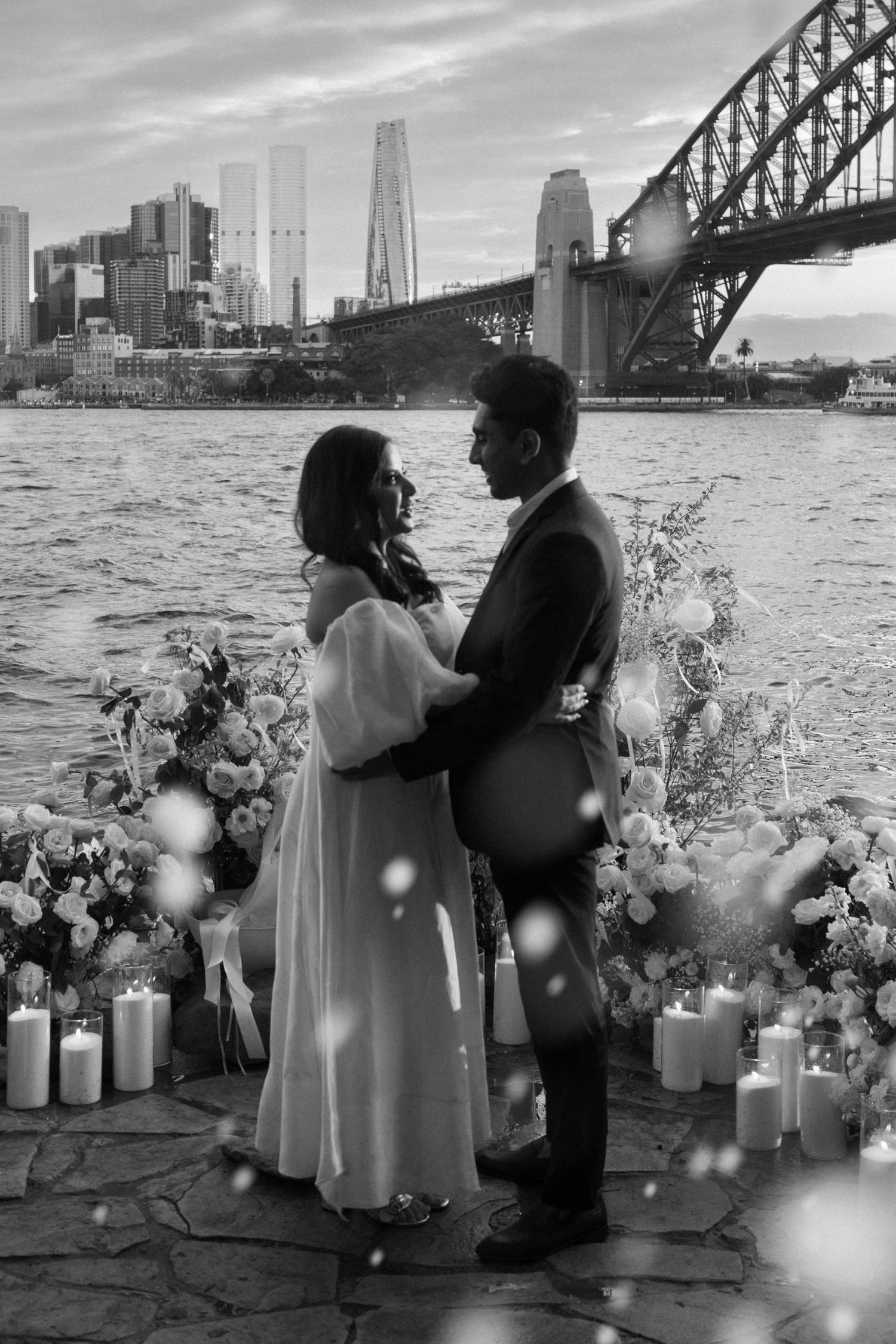A romantic black and white engagement photo sequence by the Sydney Harbour Bridge with floral arrangements and candles.