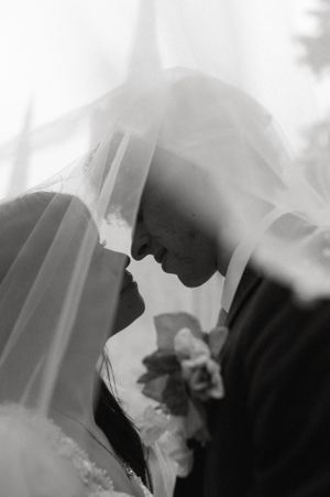 A romantic black and white wedding portrait showing a close moment between newlyweds beneath a flowing veil.