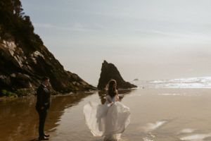 Two people walking on a misty beach with dramatic cliffs and waves at sunset by the Oregon coast.
