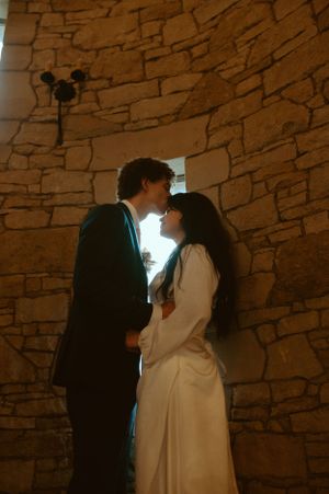 A romantic moment between newlyweds in a rustic stone archway with warm lighting.