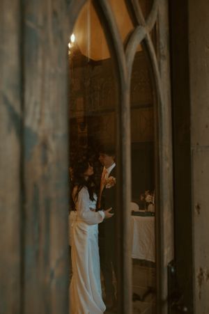 A wedding couple shares a tender moment in a gothic church archway with dramatic lighting.
