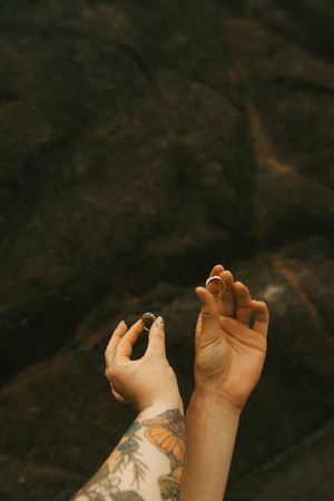 Two tattooed hands reaching upward against a dark rocky background.