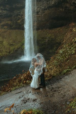 A couple shares an intimate moment near a majestic waterfall during a foggy autumn day in nature.
