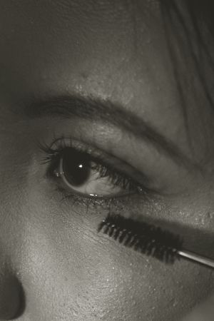 Black and white closeup shot of eye makeup application with mascara wand and long eyelashes.