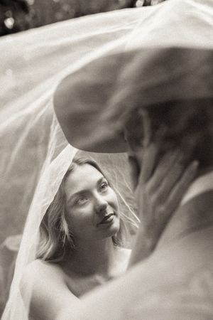 A dreamy black and white photograph showing a person through sheer white veil fabric creating an ethereal effect.