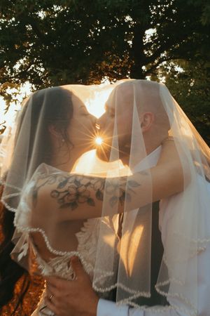 Sun flares through a white veil during an intimate outdoor moment at sunset.