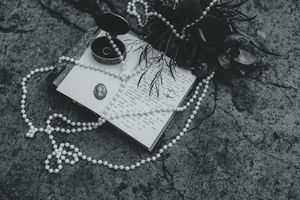 Black and white photograph of scattered pearls, letters, and vintage items arranged on a textured surface.