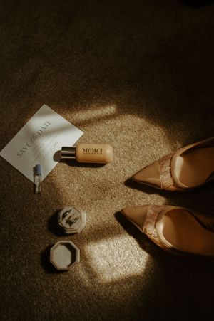 Wedding accessories including perfume bottle and beige heels arranged in dramatic lighting.