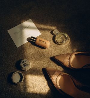 Elegant beige flats and personal items arranged in dramatic light on textured carpet, creating a moody still life scene.